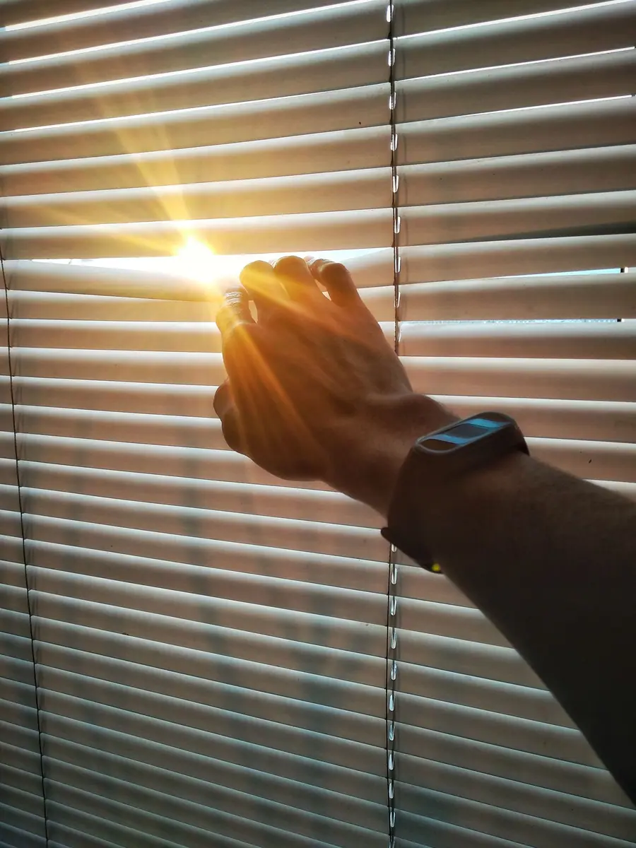Hand parting window blinds with bright sun flaring through