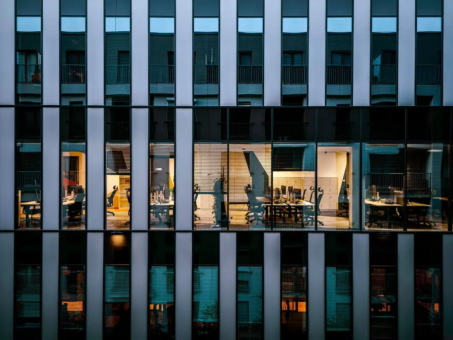 Office building facade at dusk with a lit floor of desks behind the glass
