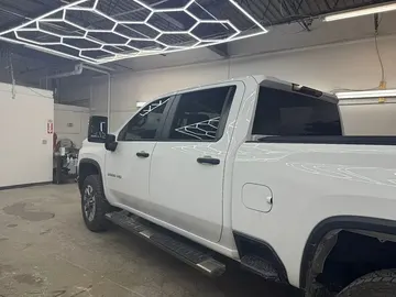 White Chevy Silverado HD pickup with tinted windows in a shop