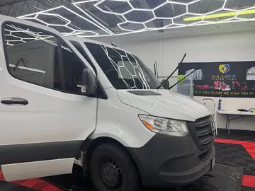 White Mercedes Sprinter van with tinted windows under hexagon lights in the shop